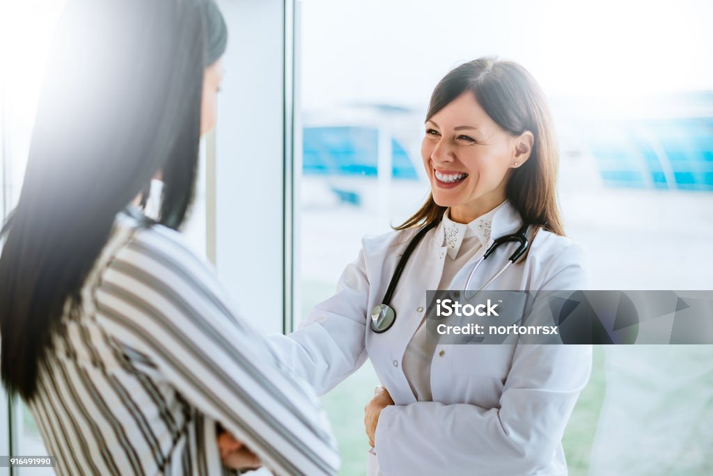 Cheerful doctor talking with her patient near window. Doctor Stock Photo