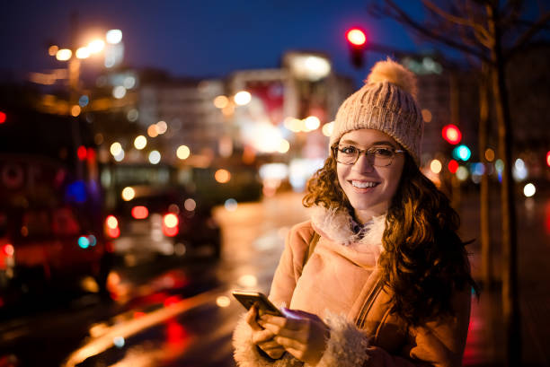 istock Young beautiful woman using phone at night outdoors, city traffic light on background. 916492004