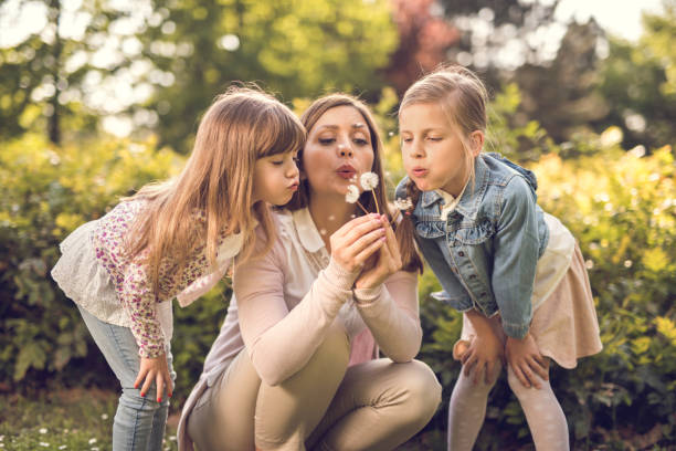Mother blowing at dandelion with two small daughters