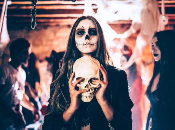 Young woman with skeleton make-up holding skull at Halloween party Young woman with santa-muerte make-up and disguise holding skull at Halloween dungeon party face paint halloween adult men stock pictures, royalty-free photos & images
