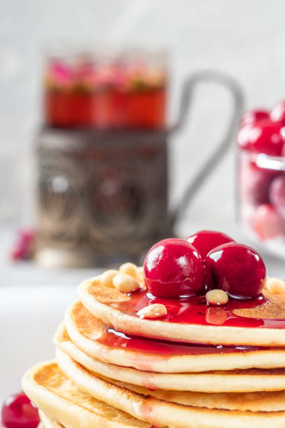 Pancakes homemade cake in stack decorated with berries frozen cherry and pine nut on white plate and  light background low key concept healthy breakfast with mug of flower tea.
