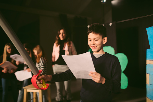 Group of children enjoying drama club rehearsal. They are reading script with their drama teacher.