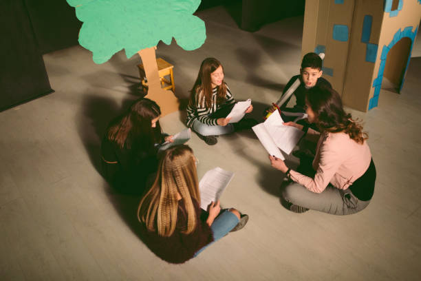 School Play Rehearsal Group of children enjoying drama club rehearsal. They are sitting and reading script with their drama teacher. rehearsal photos stock pictures, royalty-free photos & images