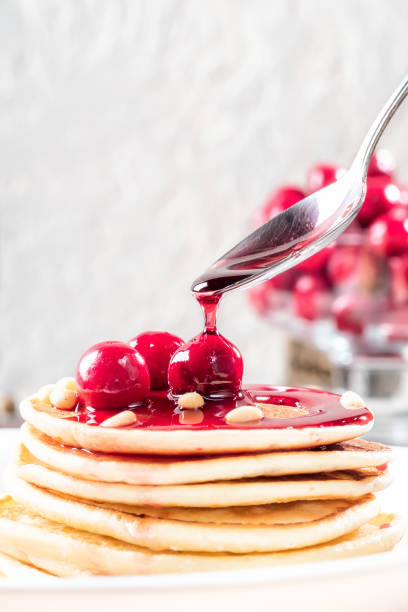 bolo caseiro de panquecas na pilha, decorada com morangos congelados cereja e porca de pinho branco placa polvilhar com xarope de cereja - maple keys fotos - fotografias e filmes do acervo