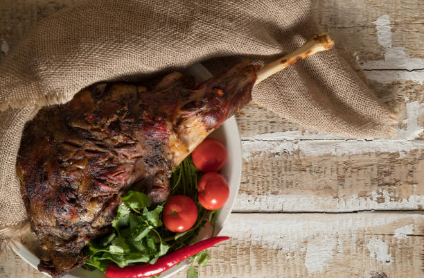 жареное мясо ноги ягненка запеченные целом лежит со свежей томатной зеленью и горячим перцем на блюде - lamb shank roast lamb leg of lamb стоковые фото и изображения