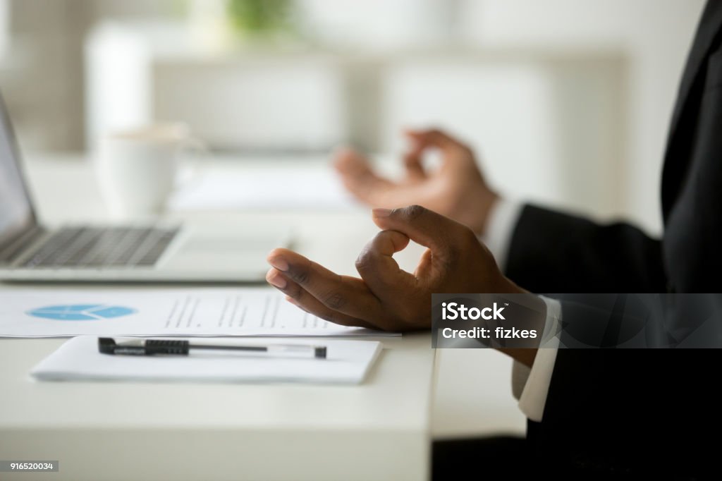 African-american businessman in suit meditating in office, close up view African american calm businessman relaxing meditating in office, peaceful ceo in suit practicing yoga at work, focus on black man hands in mudra, successful mindful people habits concept, close up Working Stock Photo