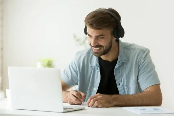 Photo of Smiling man wearing headphones looking at computer screen making videocall