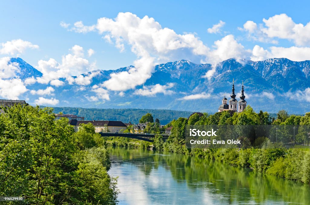 The Alps in Villach - mountain view with the clouds The Alps in Villach - mountain range in the clouds with a small chapel on the bank of the river Villach Stock Photo
