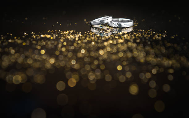 primo piano paio di fedi nuziali in platino con diamante su sfondo riflesso bokeh - jewelry gem gold reflection foto e immagini stock