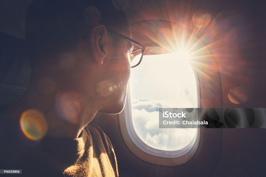 Traveling by airplane Young man looking out through window of the airplane during beautiful sunrise. Airplane Stock Photo