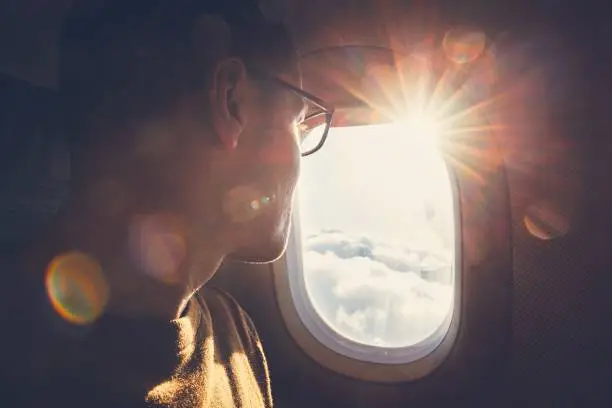 Young man looking out through window of the airplane during beautiful sunrise.