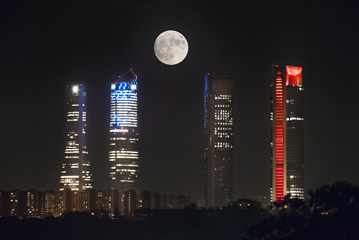 Full moon over Cuatro Torres business area skyline at night in Madrid, Spain.