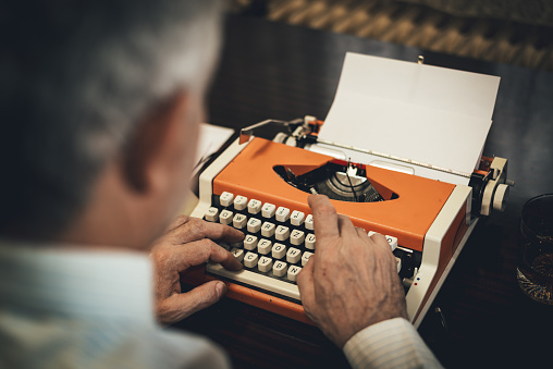 Rear view of a senior men's hands typing on obsolete typewriter.