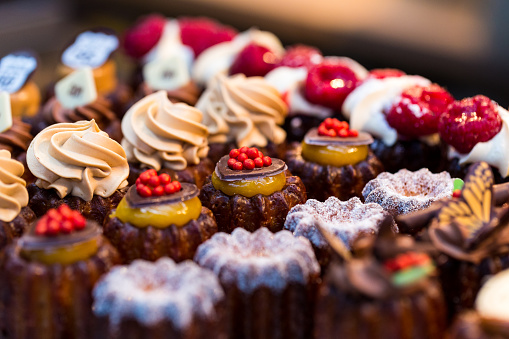 Close up horizontal color image depicting a selection of freshly baked delicious cakes and cupcakes for sale at Borough Market in London, one of the oldest and most popular food markets in the world. The gourmet cakes are topped with all kinds of things, including whipped cream and fresh strawberries. Room for copy space.