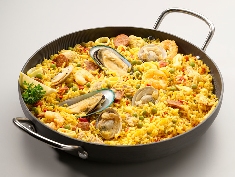 A large paella pan with brown rice, lemon, seafood and small tomatoes. You can see scampi, mussels and mussel shells. The pan looks very used.