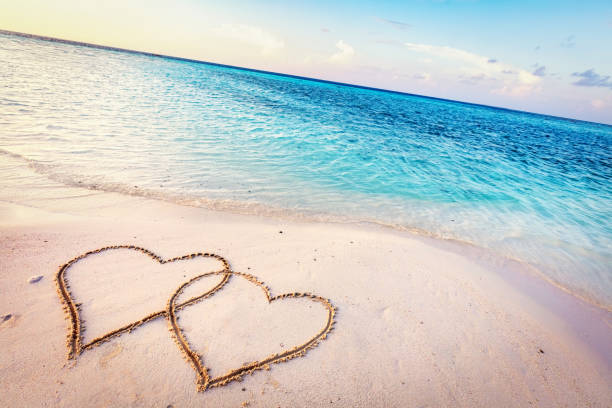 istock Two hearts drawn on sand of a tropical beach at sunset. 916582442