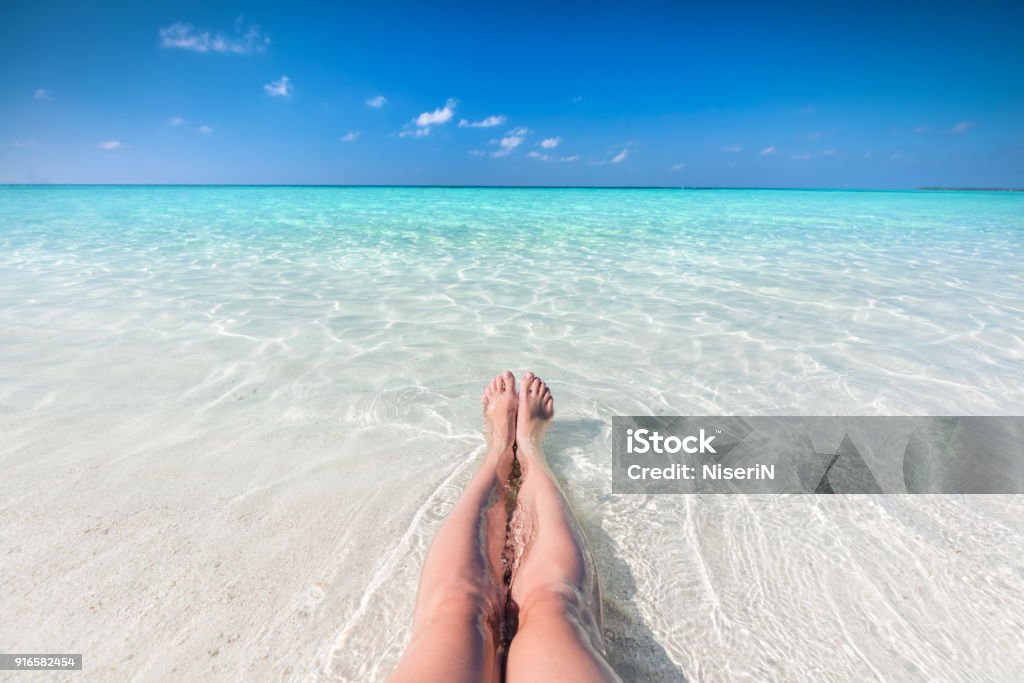 Vacation on tropical beach in Maldives. Woman's legs in the clear ocean Vacation on tropical beach in Maldives. Woman's legs in the clear ocean water. First person perspective Beach Stock Photo