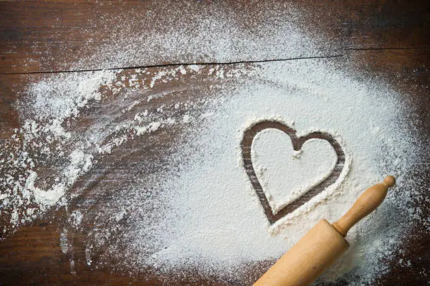 Baking background with the rolling pin, heart shape and flour on the wooden table. Copy space for text. Top view