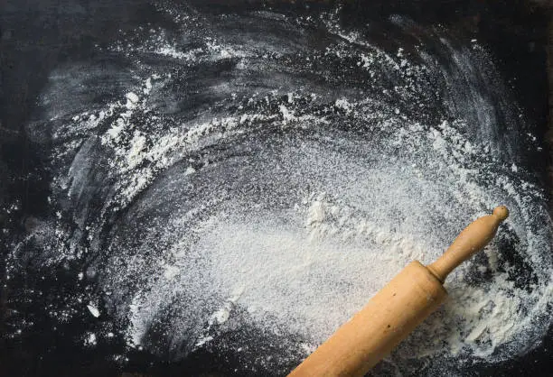 Baking background with the rolling pin and flour. On the dark table. Copy space for text. Top view