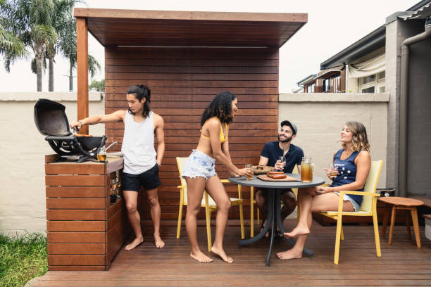 Group of young people having bbq on decking with alcoholic drinks Young men and women talking and relaxing outside, Japanese man cooking on barbecue, three friends at table talking drinks on the deck stock pictures, royalty-free photos & images