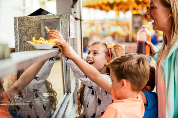 Buying Food at the Fairground Children with their mother getting some food at a fairground. They are buying french fries at a fast food van. concession stand stock pictures, royalty-free photos & images