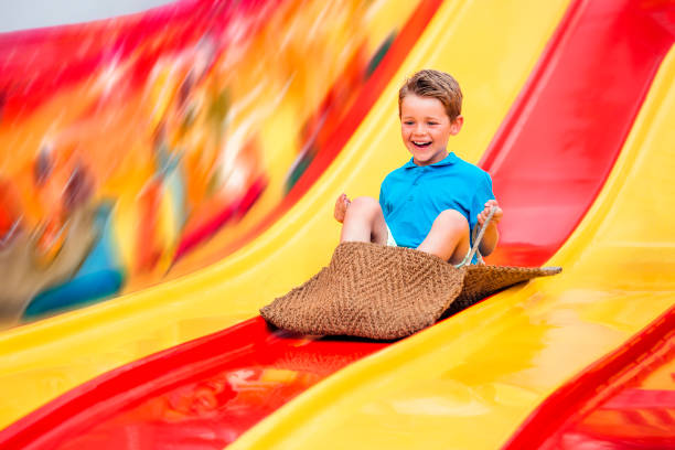 Happy toddler joyfully playing on a vibrant red slide in an indoor playground, surrounded by colorful play areas and laughter