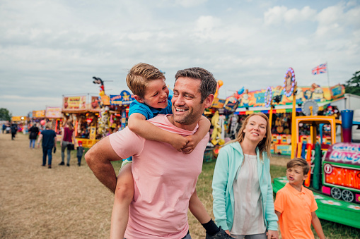 Family enjoying time at the fairground. Dad is carrying his son on his back