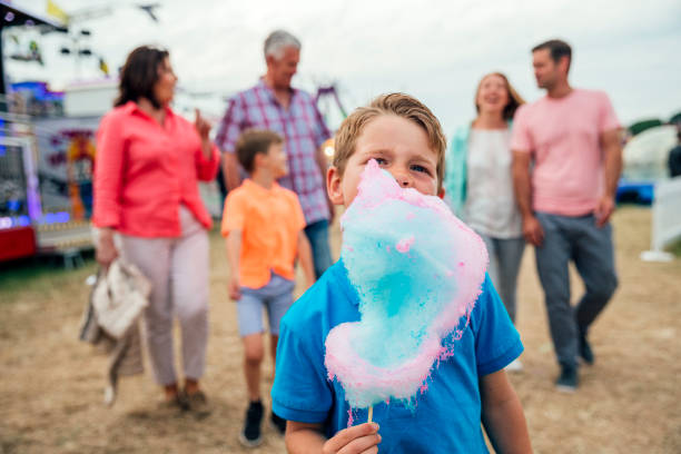 Little boy Eating Cotton Candy at the Fairground Multi-generation family visit the fairground to enjoy the rides together. Little boy is seen in the foreground eating cotton candy child cotton candy stock pictures, royalty-free photos & images