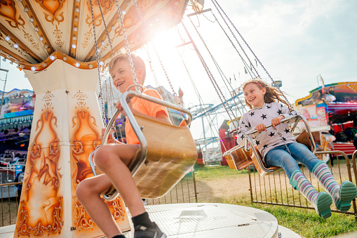 Adorable little preschool girl with glasses riding on animal on roundabout carousel in amusement park. Happy healthy baby child having fun outdoors on sunny day. Family weekend or vacations.