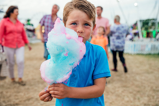 Multi-generation family visit the fairground to enjoy the rides together. Little boy is seen in the foreground eating cotton candy