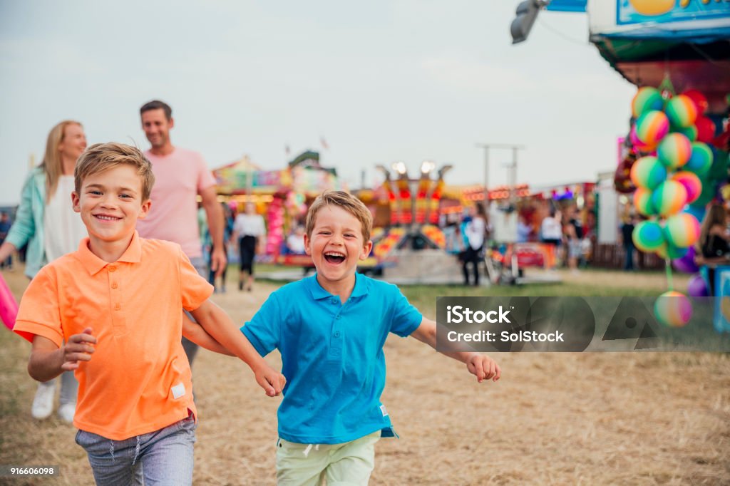 Family Day Out at the Fairground Family visit the fairground to enjoy the rides together. Little boys are running towards the camera. Parents walking behind. Family Stock Photo