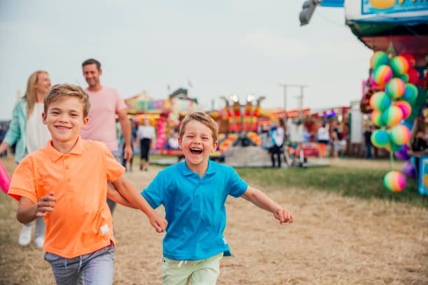 Family Day Out at the Fairground Family visit the fairground to enjoy the rides together. Little boys are running towards the camera. Parents walking behind. carnival stock pictures, royalty-free photos & images