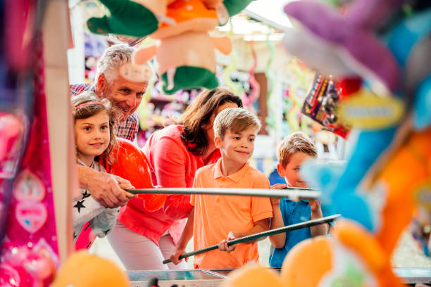 Multi Generation Family Playing Hook a Duck Grandparents helping their grandchildren hook a duck on a side show at a fairground duck family stock pictures, royalty-free photos & images