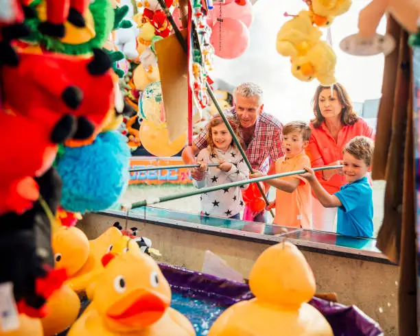 Grandparents helping their grandchildren hook a duck on a side show at a fairground
