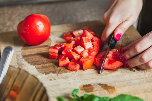 Cutting salad. The woman's hand slices the ripe red tomato into cubes. Nearby is a whole tomato