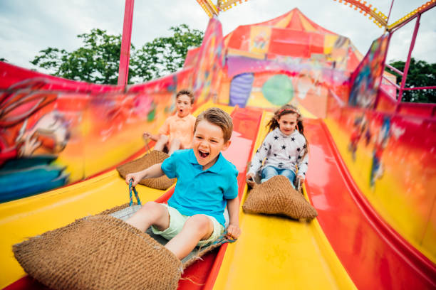 Children on Slide at a Funfair Children having fun sliding down a yellow and red slide while sitting in  burlap sacks carnival children stock pictures, royalty-free photos & images