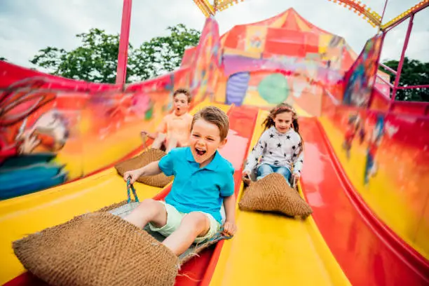 Children having fun sliding down a yellow and red slide while sitting in  burlap sacks