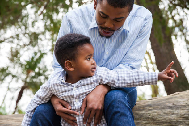 istock Dad talking to his little son while sitting on a log. 916607808
