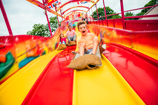 Little boy having fun sliding down a yellow and red slide while sitting in a burlap sack