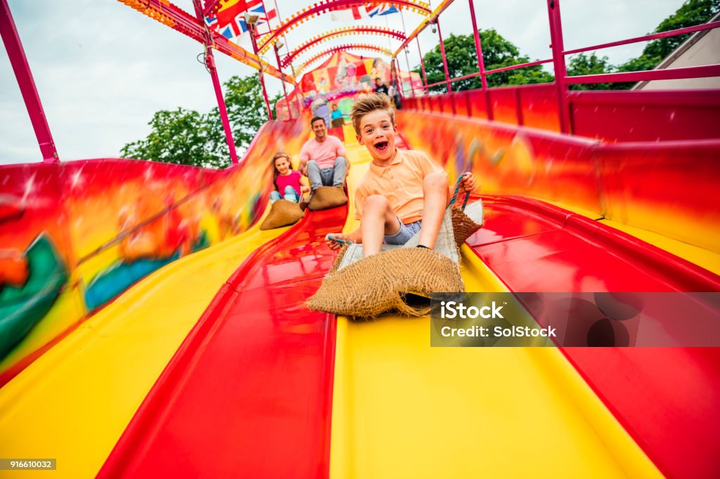 Little boy on Slide at a Funfair Little boy having fun sliding down a yellow and red slide while sitting in a burlap sack Family Stock Photo