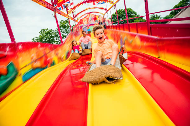 Little boy on Slide at a Funfair Little boy having fun sliding down a yellow and red slide while sitting in a burlap sack fun ride stock pictures, royalty-free photos & images