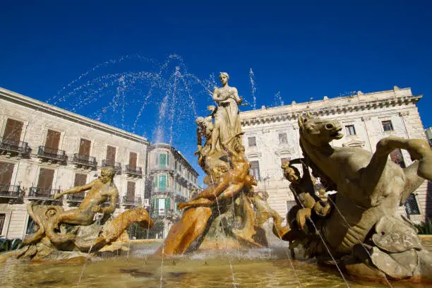 Ortygia, Siracusa, Sicily: Fountain of Diana (constructed 1906) with spraying water on Piazza Archimede in Siracusa, Sicily. Backdropped by a bright blue sky.