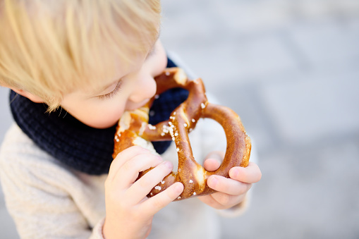 Little tourist holding traditional bavarian bread called pretzel on the town hall building background in Munich, Germany. Preschooler boy enjoy travel with his parents