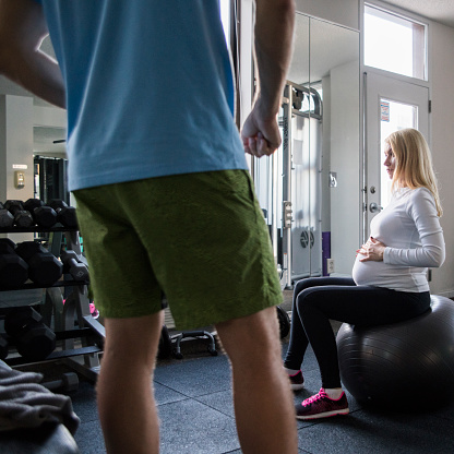 Pretty pregnant woman exercising in the gym with the gymnastic ball under curation of the personal trainer