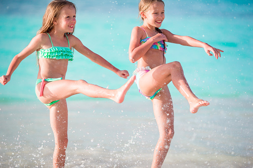 Little girls having fun at tropical beach playing together at shallow water. Adorable little sisters at beach during summer vacation