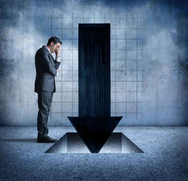 istock Businessman Stands With Head In Hand Looking At Falling Arrow 916713848