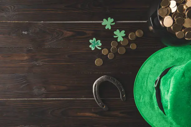 Photo of top view of pot with golden coins, horseshoe and green hat on wooden table, st patricks day concept