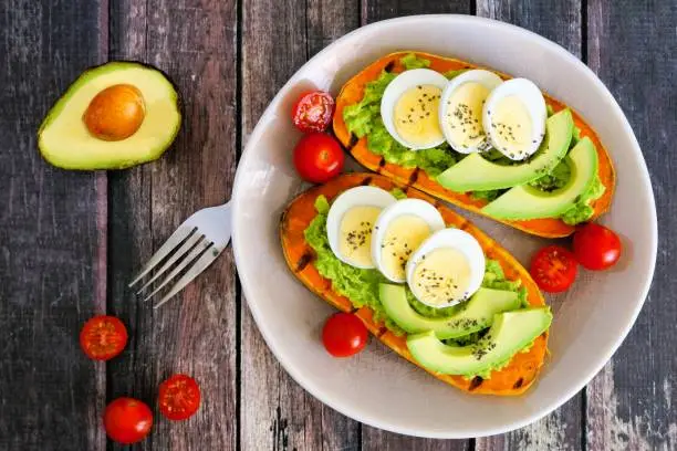 Sweet potato toasts with avocado, eggs and chia seeds on a plate. Top view on a dark wood background.