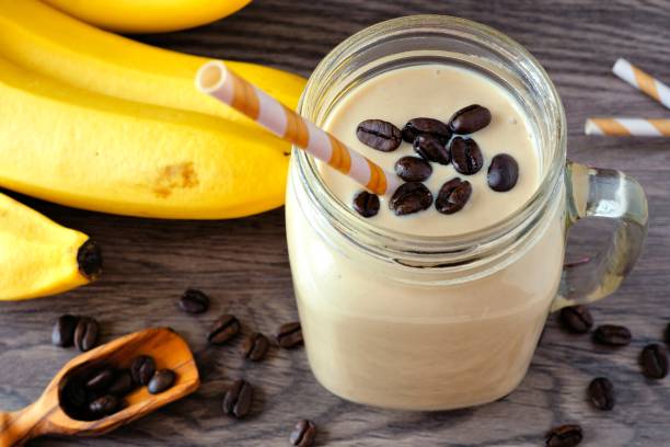 Coffee, banana smoothie in a mason jar. Above view over a rustic wood background.