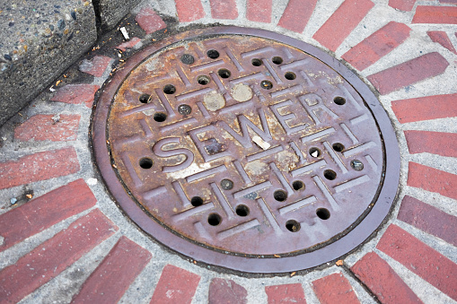Distressed sewer manhole cover on brick city street.